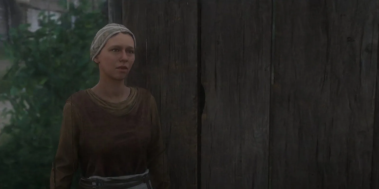 Martha, vợ thợ rèn, đứng trước cửa nhà trong Kingdom Come Deliverance 2